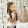 A young girl helps her mother try on glasses in a stylish optical store.