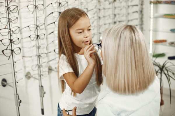 A young girl helps her mother try on glasses in a stylish optical store.