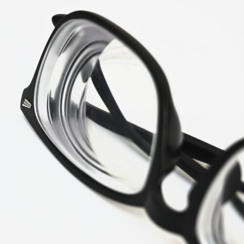 Modern black frame eyeglasses close-up on white surface, showcasing stylish eyewear design.